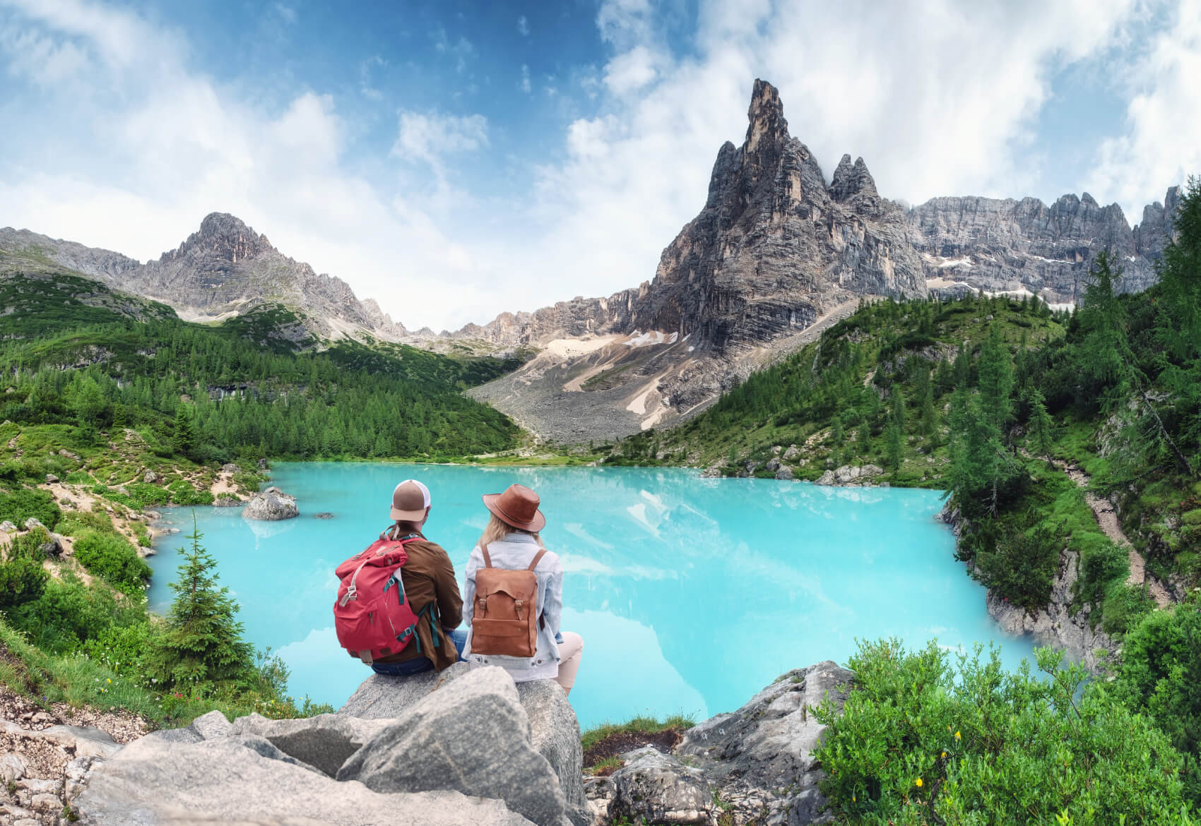 a couple of people sitting on a rock overlooking a lake and mountains