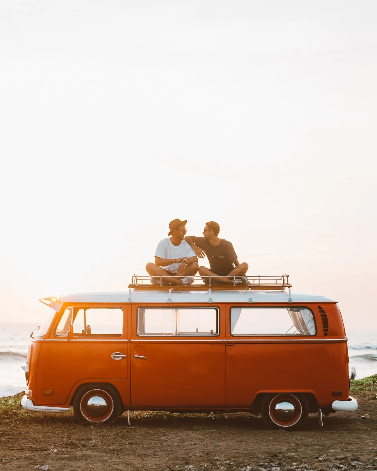 Millennials enjoying adventure travel on top of a vintage orange Volkswagen van near the beach.